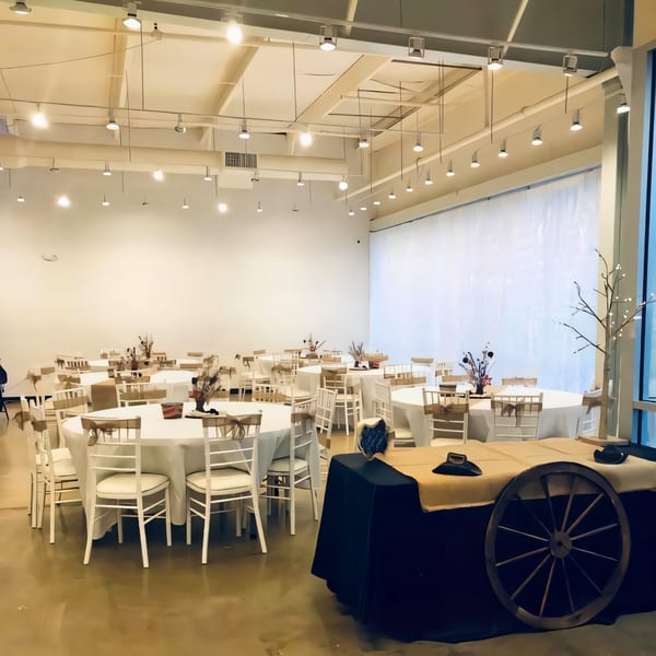 Spacious event room with round tables, white chairs, and a decorative wagon wheel display at Mango's Mexican Restaurant.