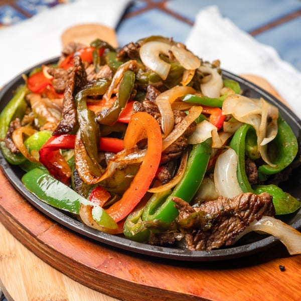 Sizzling beef fajitas with colorful bell peppers and onions in a cast iron skillet on a wooden board.