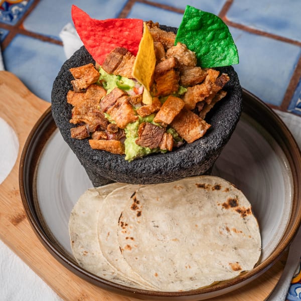 Guacamole with chicharrones and colorful tortilla chips in a molcajete, served with tortillas.