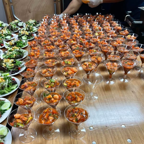 Numerous martini glasses filled with shrimp ceviche and plates of green salad on a wooden table.