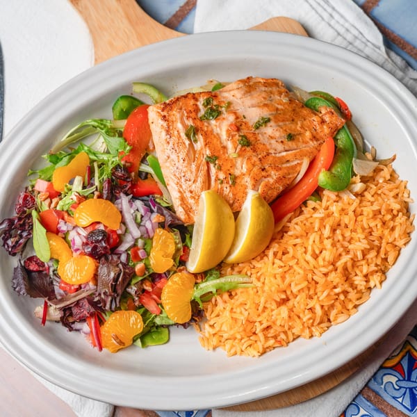 Grilled salmon with bell peppers, onions, rice, and a colorful salad with mandarin oranges and cranberries.
